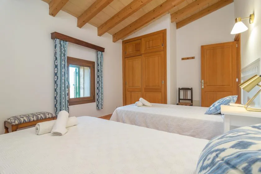 A bedroom with two beds, wooden doors, and a window with patterned curtains.