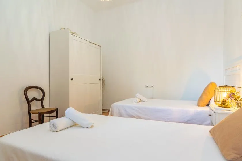 A bedroom with two beds and a small chair beside a wardrobe.