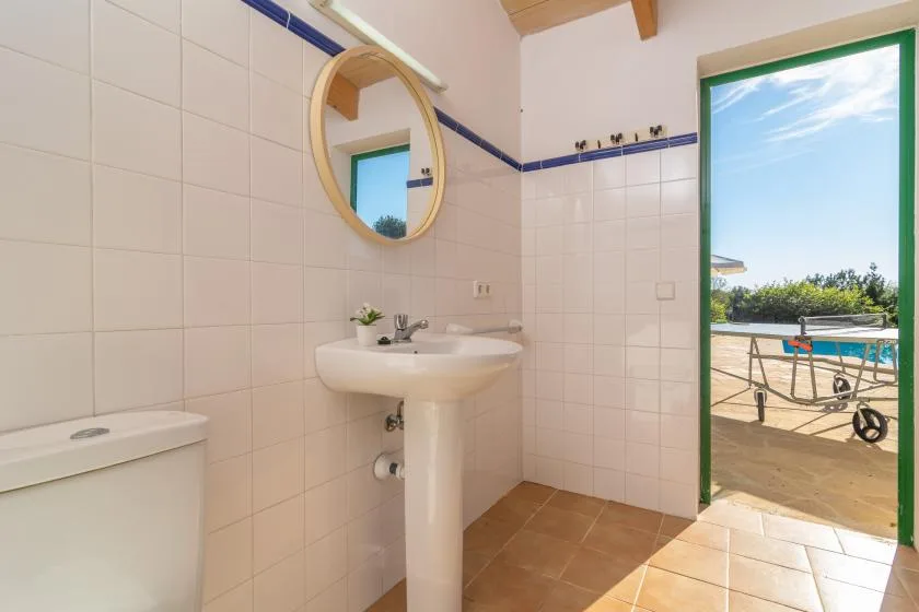 A tiled bathroom with a pedestal sink and an open doorway to an outdoor patio.