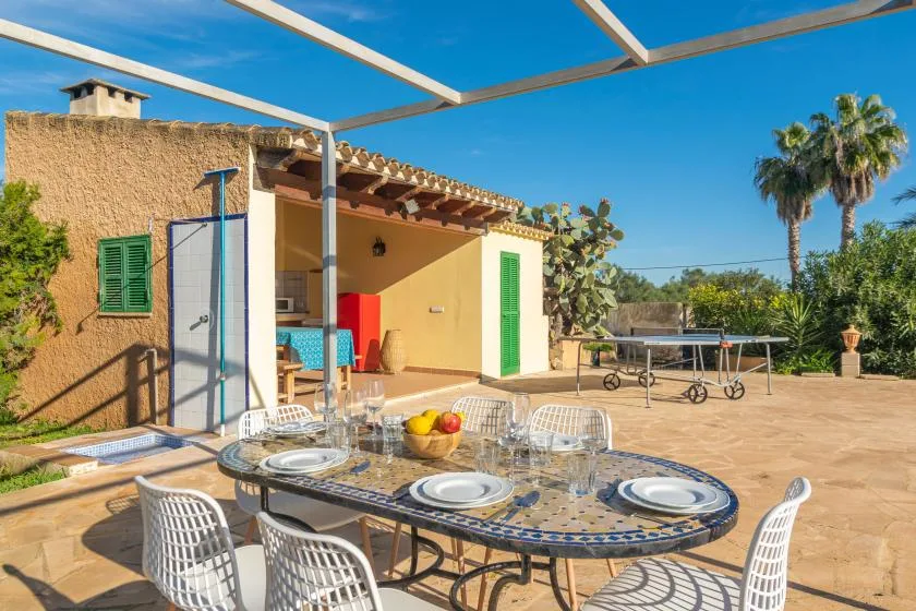 An outdoor dining area with a tiled table and seating beneath a pergola.