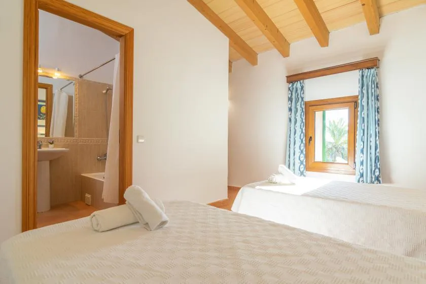 A bright bedroom with two beds, exposed wooden ceiling beams, and a window.