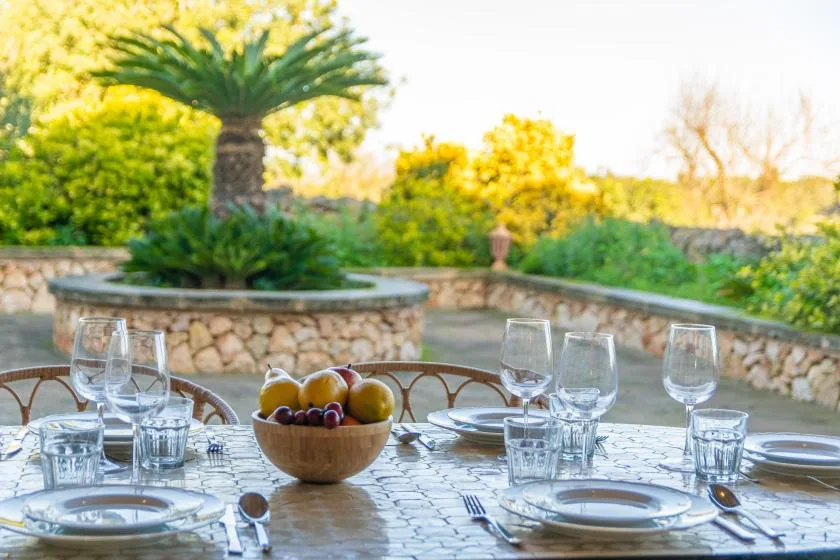 An outdoor dining table set with glassware overlooks a lush garden.