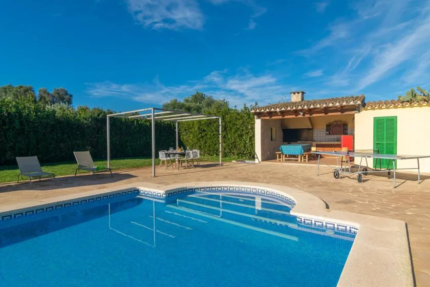A swimming pool and patio sit beside a small house and outdoor dining area.