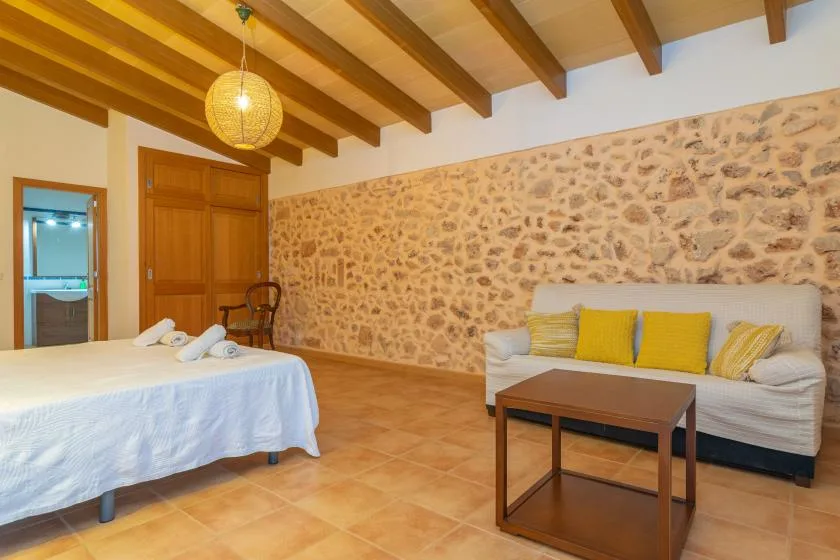 A bedroom with a bed, sofa, and wooden ceiling beams.