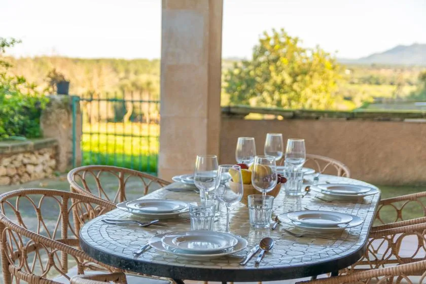 A dining table set with dishes and glassware sits on a terrace overlooking greenery.