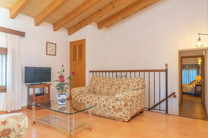 A living area with floral seating, a glass coffee table, and exposed wooden ceiling beams.