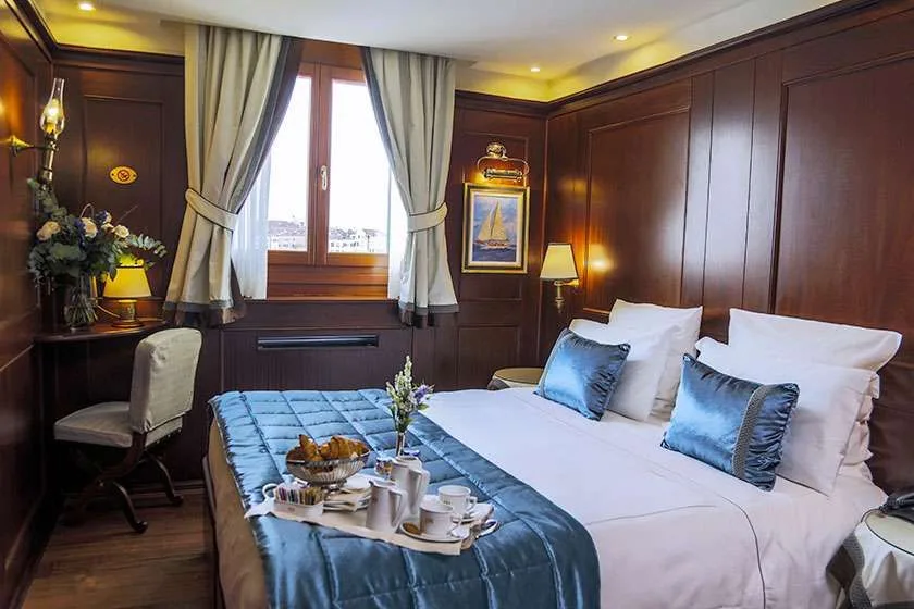 Dormitorio de hotel con revestimiento de madera oscura, cama y ventana.