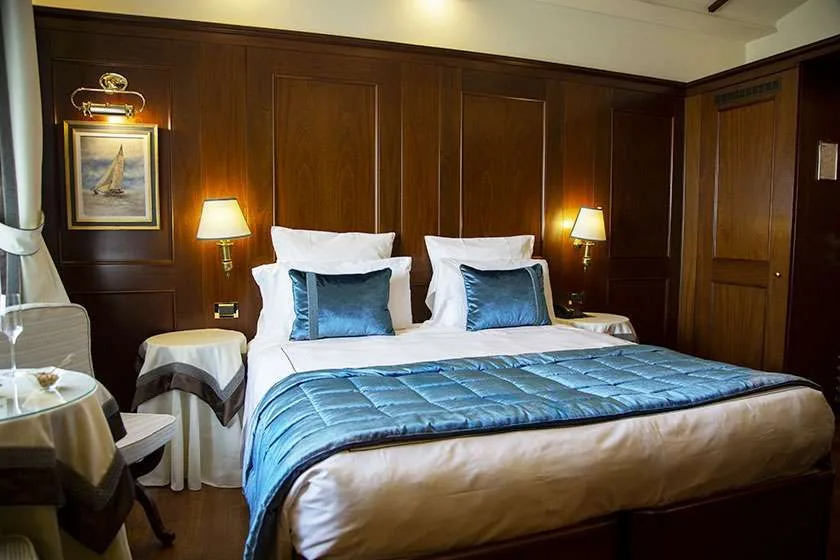 Habitación de hotel con cama, revestimiento de madera oscura y apliques de pared.