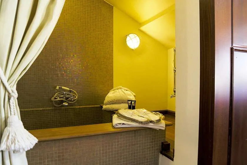 Baño con bañera, cortina, toallas y un aplique circular.
