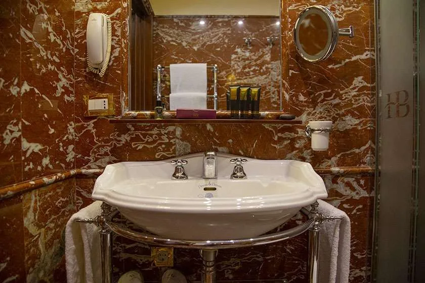 Lavabo de baño junto a paredes de mármol rojo.