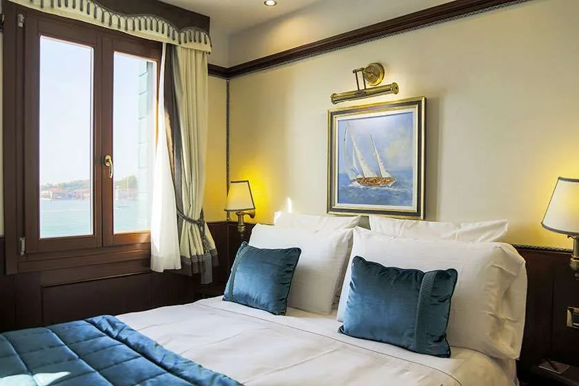 Habitación con cama, ventana con vistas al agua y un cuadro de un velero.
