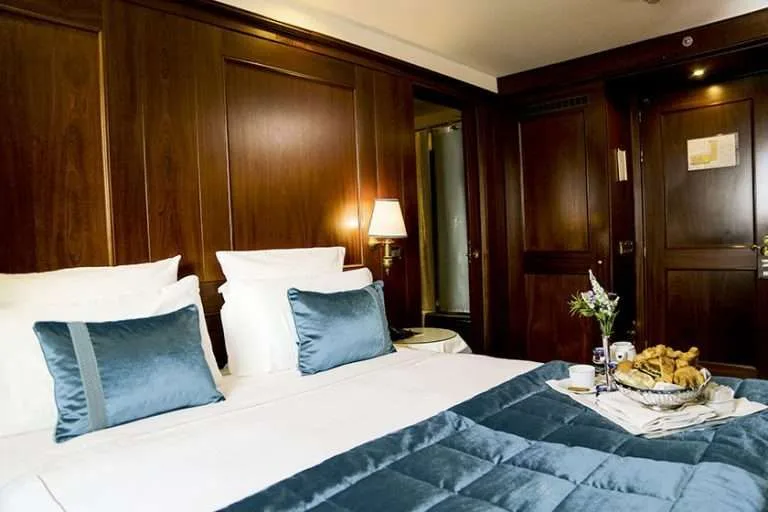 Habitación de hotel con cama, revestimiento de madera oscura y detalles en verde azulado.