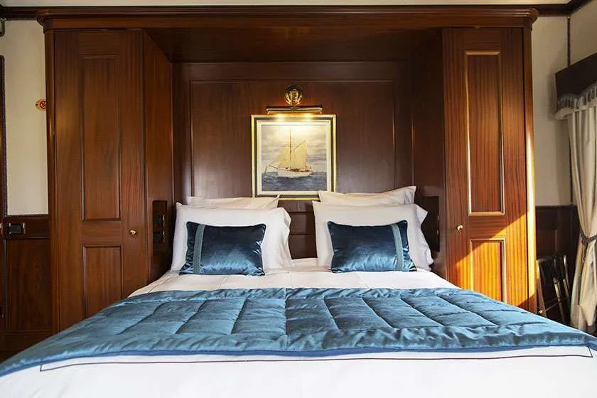Cama enmarcada por armarios de madera oscura y un cuadro de temática náutica.
