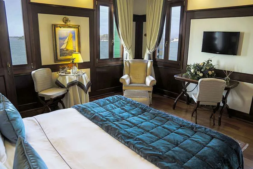Habitación de hotel con cama, zona de estar, escritorio y ventanas con vistas al agua.