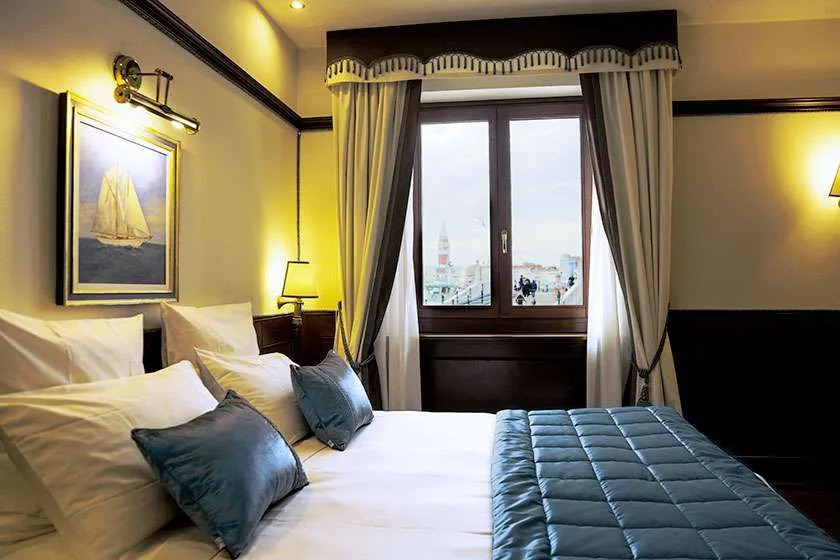 Habitación de hotel con cama y ventana con cortinas de tonos neutros.
