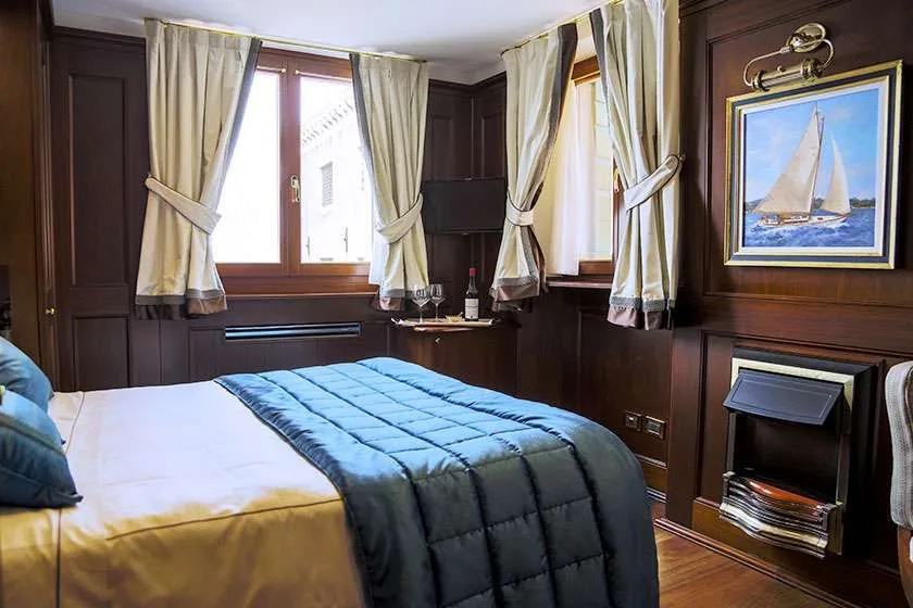 Habitación de hotel revestida de madera con cama, cortinas y una obra de un velero.