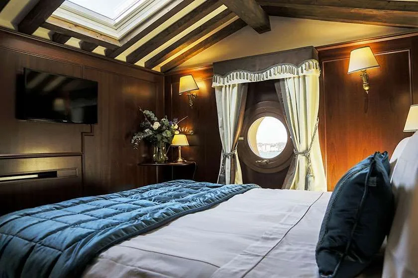 Habitación de hotel con cama, paredes de madera oscura, ventana redonda y tragaluz.