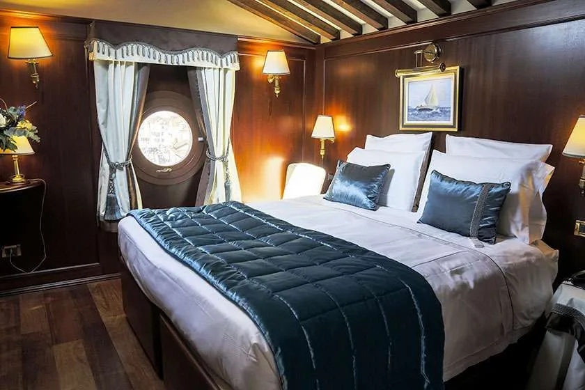 Dormitorio con revestimiento de madera oscura, ventana redonda y cama.
