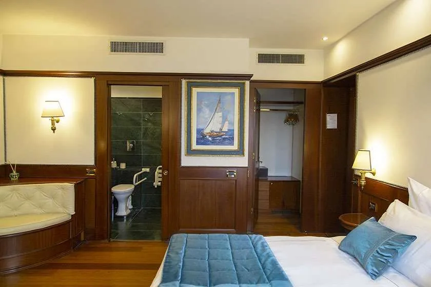 Dormitorio con cama, zona de estar, puerta del baño y una obra de temática náutica.