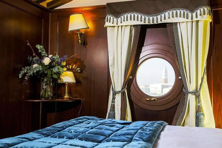 Cama azul junto a una ventana redonda con cortinas drapeadas.