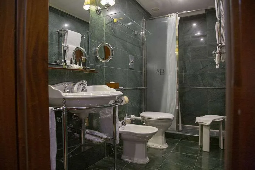 Baño con paredes de mármol verde, lavabo, bidé, inodoro y ducha.