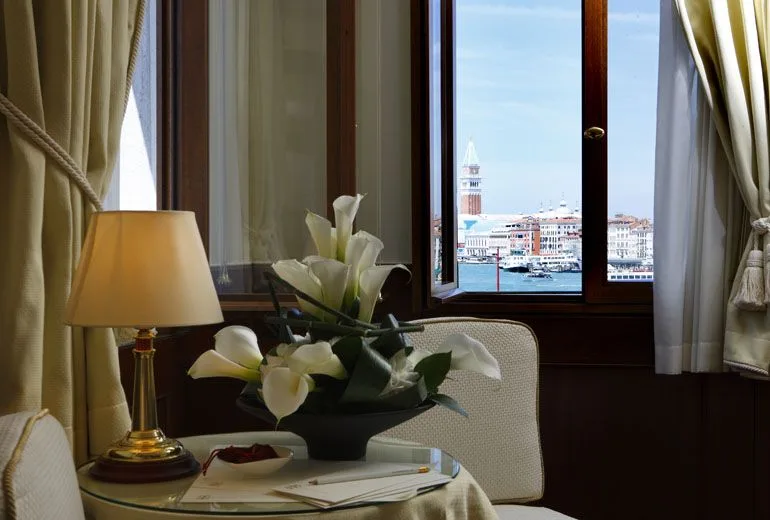 Mesa y flores junto a una ventana con vistas a Venecia y al campanario de San Marcos.