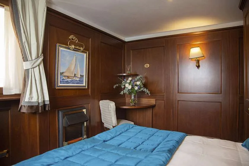 Habitación revestida de madera con cama, silla, escritorio y un cuadro de un velero.