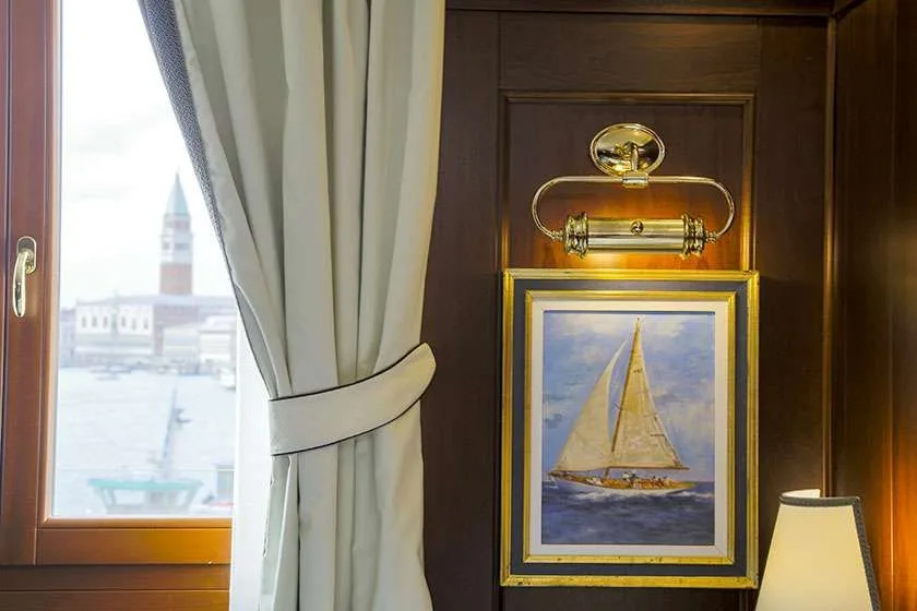 Ventana con vistas al perfil urbano de Venecia junto a una obra enmarcada de un velero.