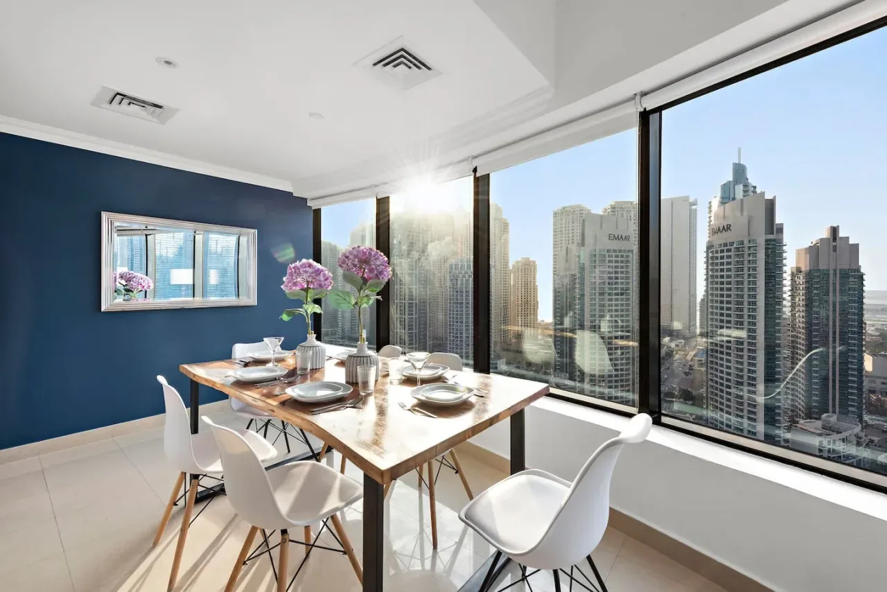 Un comedor luminoso con una mesa junto a grandes ventanales con vistas a edificios de la ciudad.