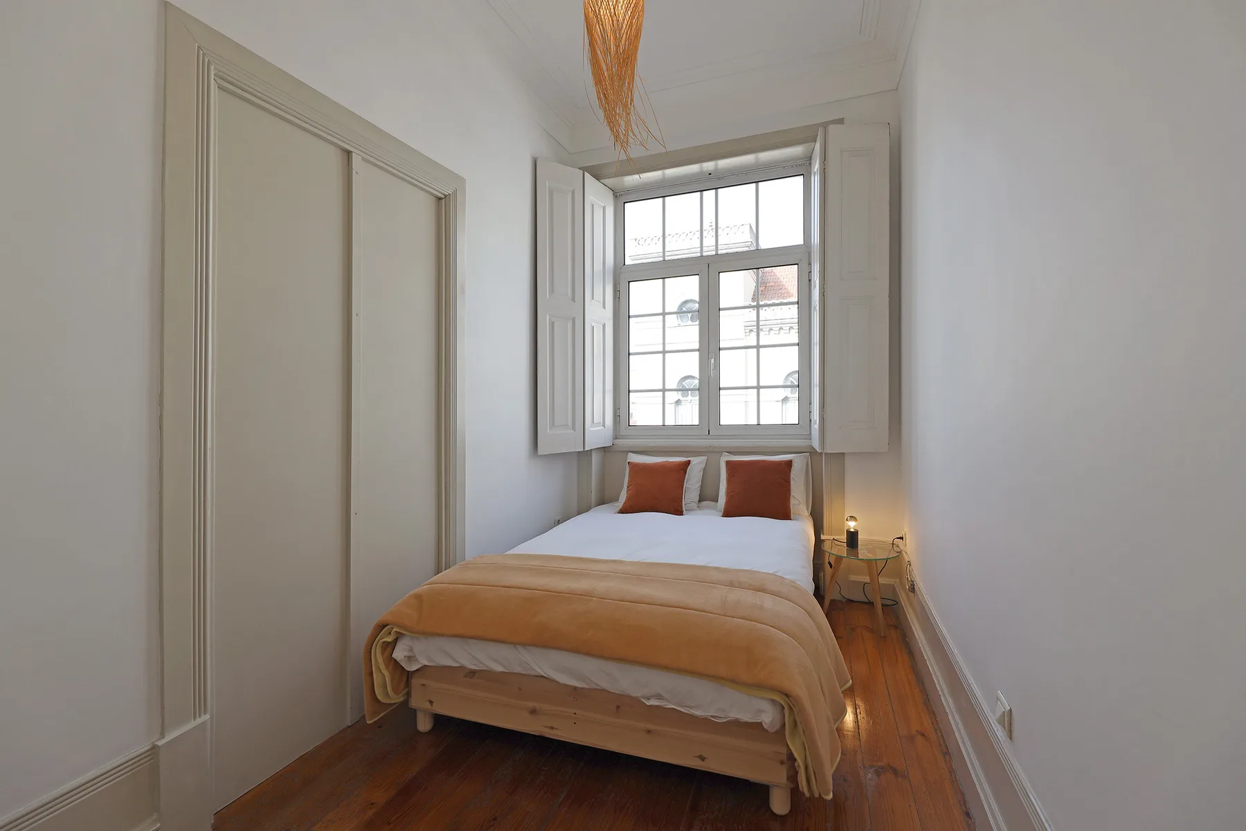 A bedroom with a bed beneath a large window with open shutters.