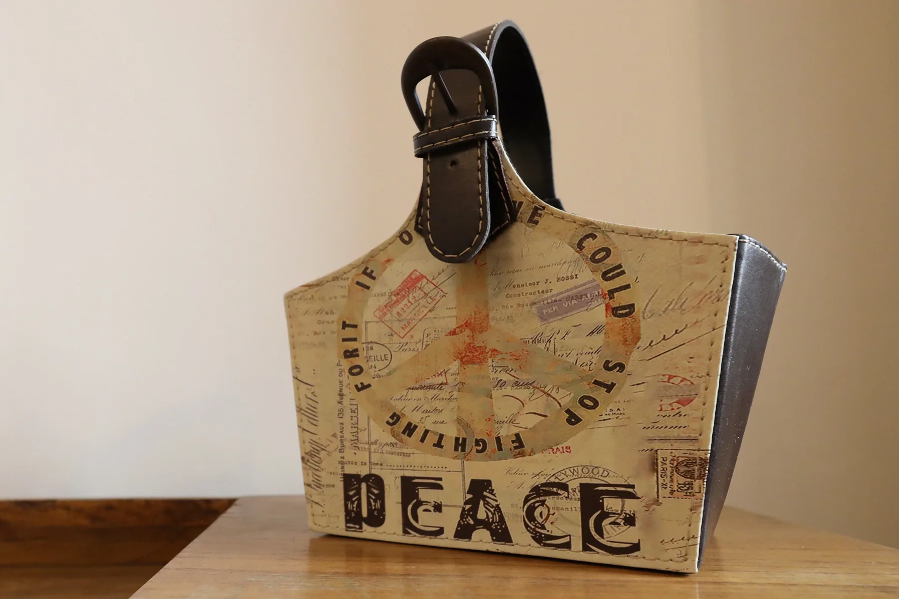 A printed tote bag sits on a wooden table against a plain wall.