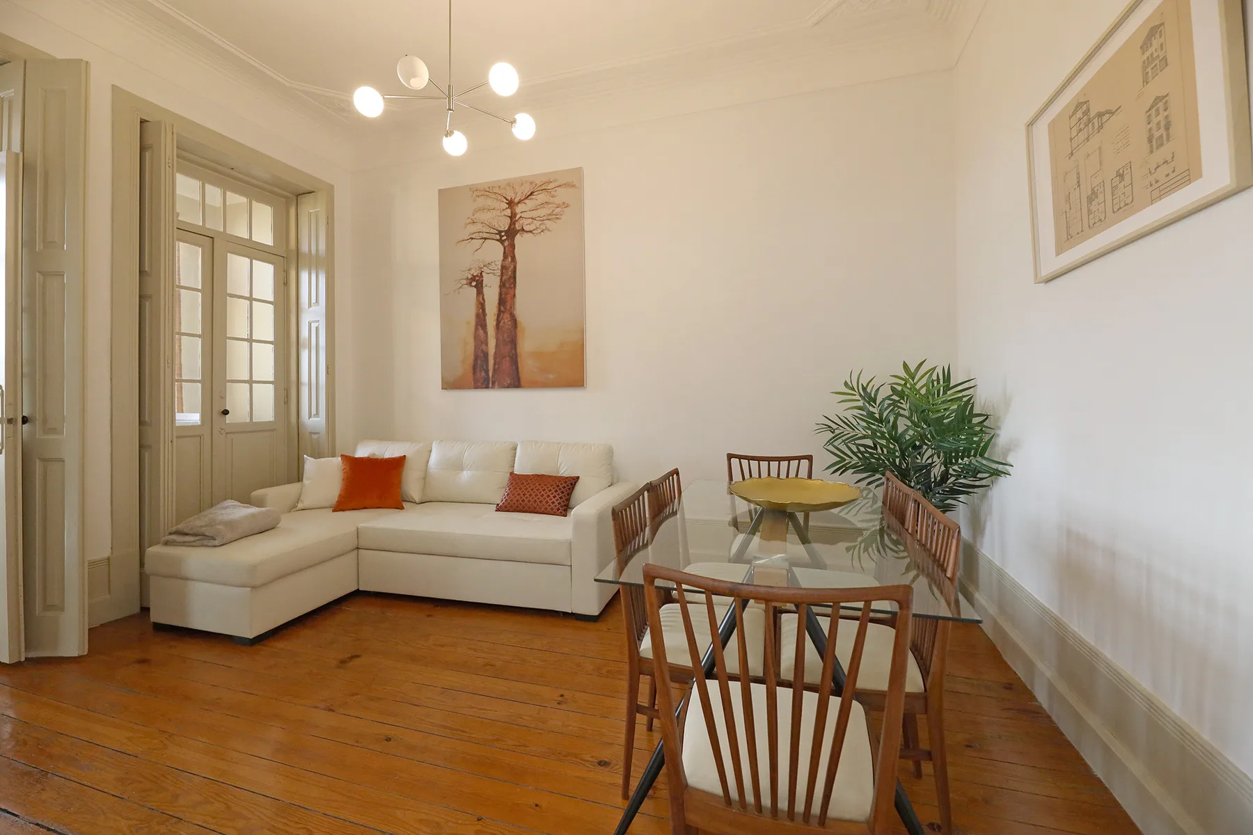 A living and dining room with seating, a glass table, and potted plants.