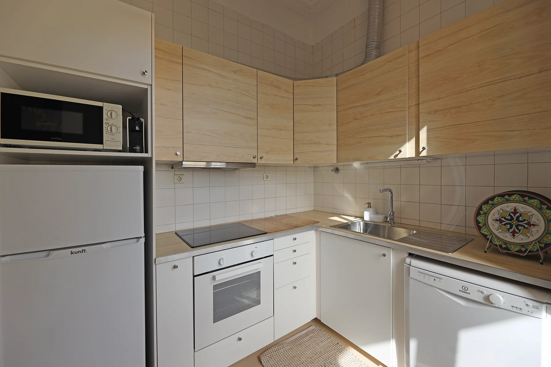 A compact kitchen with light wood cabinets, a refrigerator, and a built-in oven.