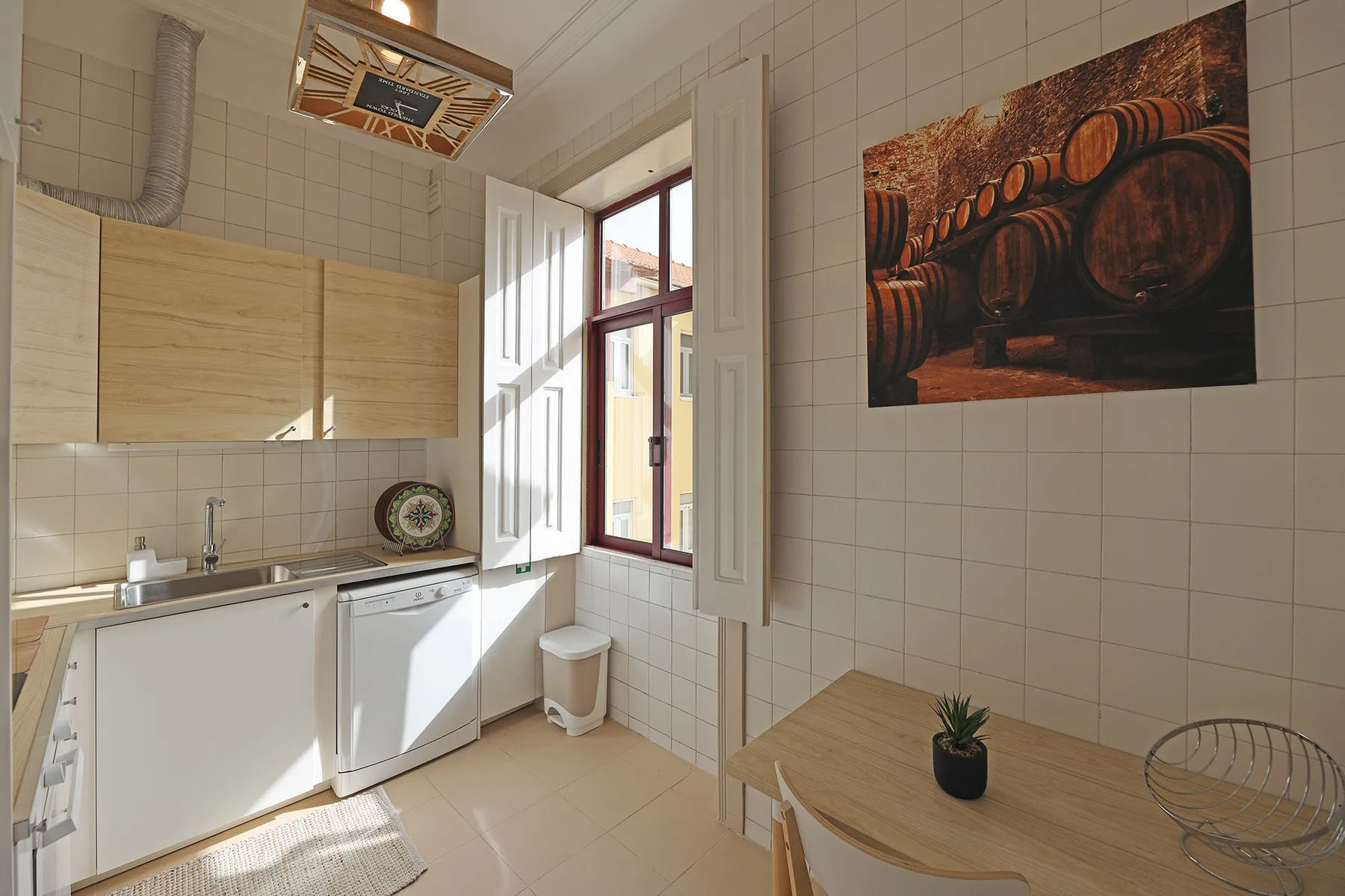 A tiled kitchen with a sink, cabinets, and a small dining table by the window.