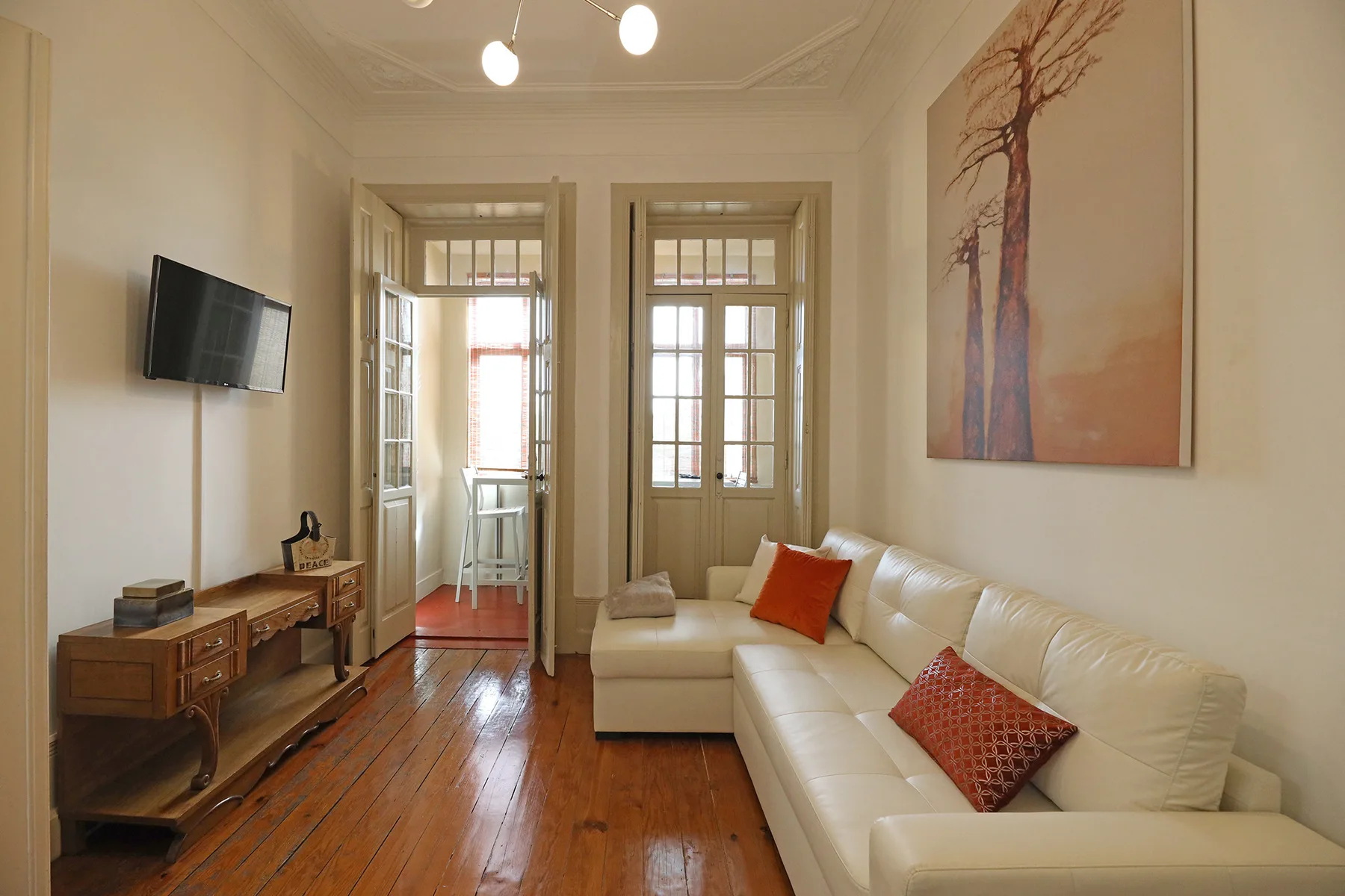 A living room with a white sofa and a television mounted on the wall.