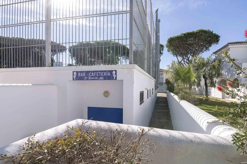 A narrow outdoor walkway runs beside a white building and fenced sports court.