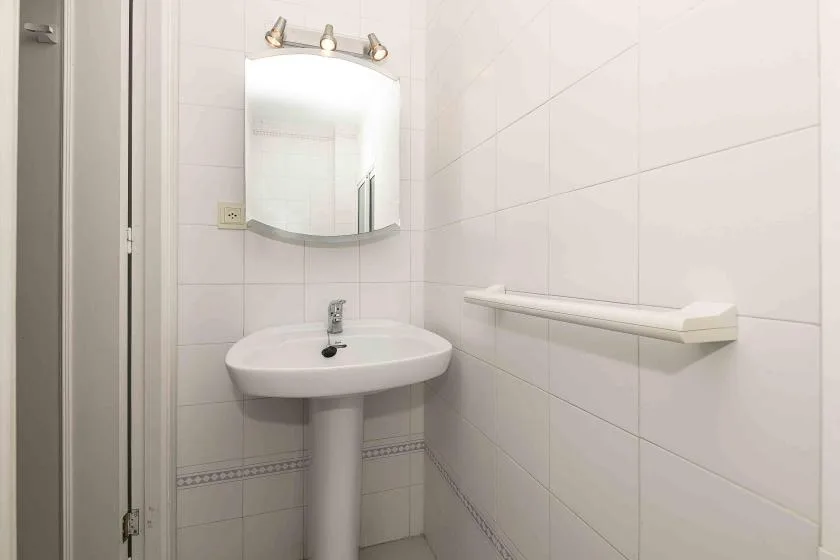 A tiled bathroom with a pedestal sink, mirror, and wall-mounted shelf.