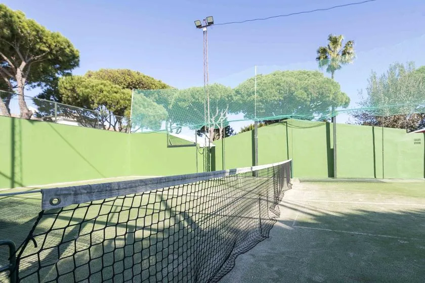 An outdoor tennis court with a net and green surrounding walls.