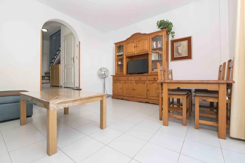 A bright living and dining area with wooden seating and a television cabinet.