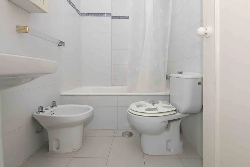 A tiled bathroom with a toilet, bidet, and shower curtain.