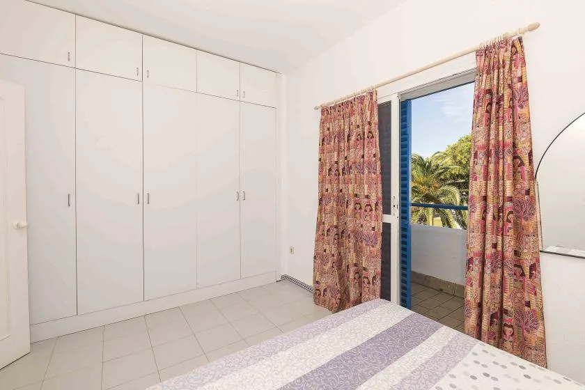 A bedroom with built-in wardrobes and a curtained opening to a balcony.