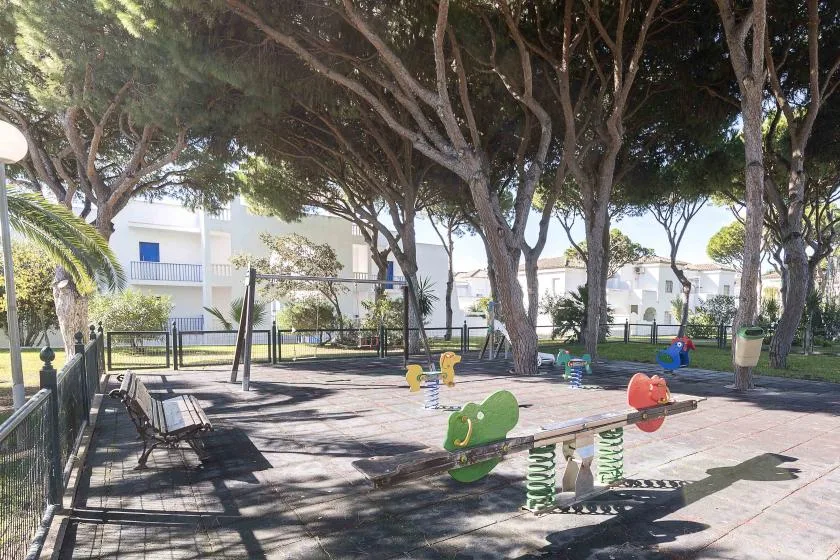 A shaded outdoor playground with spring-mounted animal rides beneath large trees.