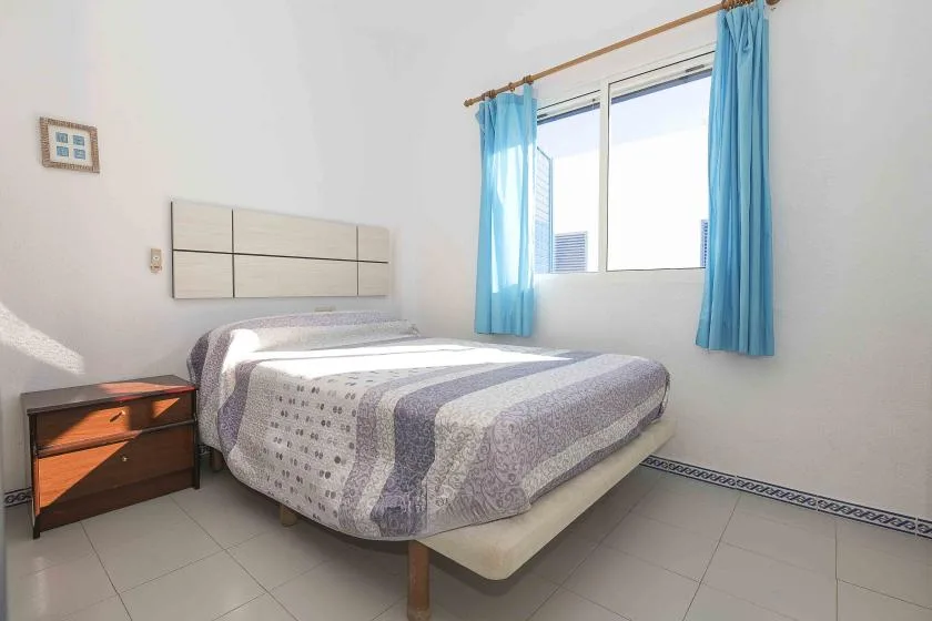 A bright bedroom with a bed beneath a window with blue curtains.