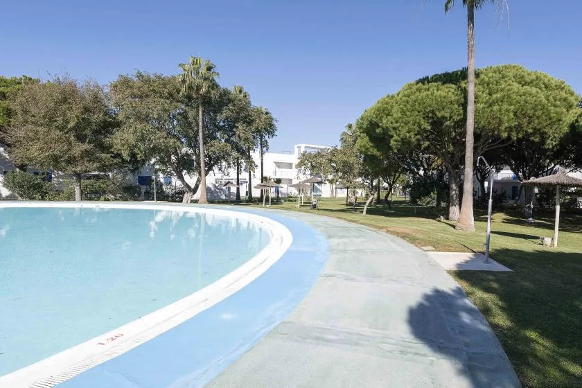 A curved outdoor swimming pool beside a paved path and landscaped grounds.