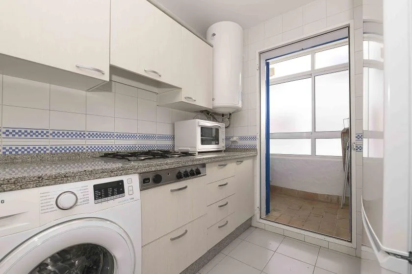 A tiled kitchen with counters, cabinets, and a washing machine beside a glass door.