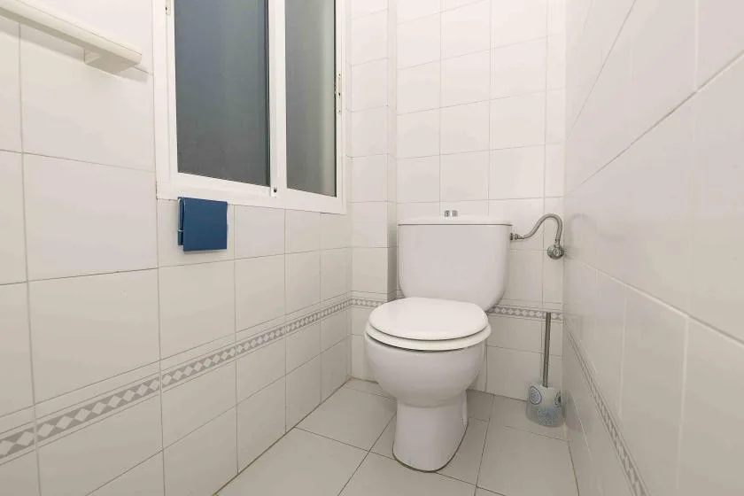A tiled bathroom with a toilet and a small window.
