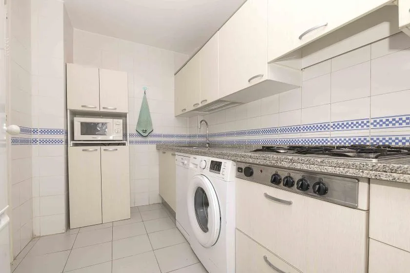 A bright tiled kitchen with white cabinets, a countertop, and laundry appliances.