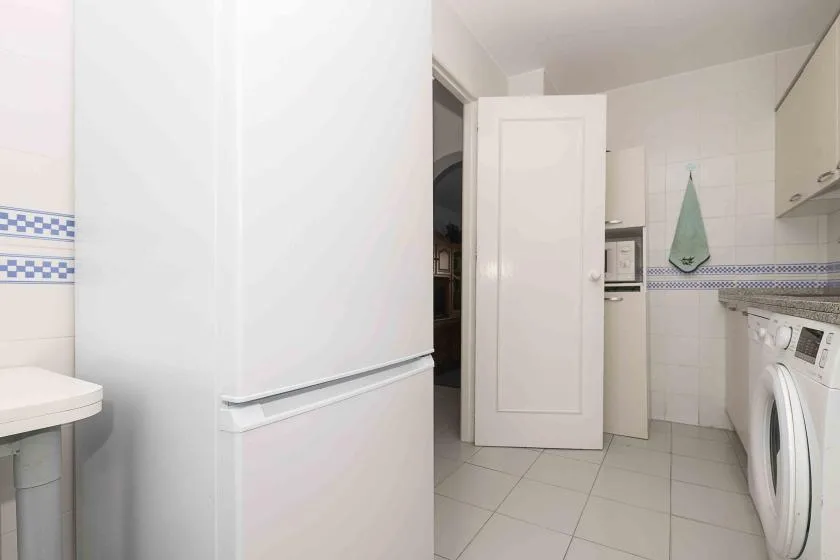 A tiled utility room with a washing machine and refrigerator.