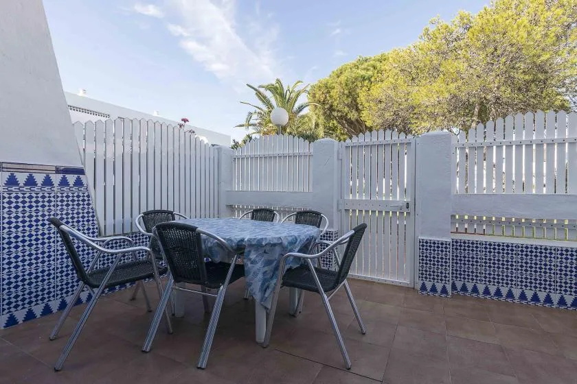 An outdoor patio dining area with a table, chairs, and a white fence.
