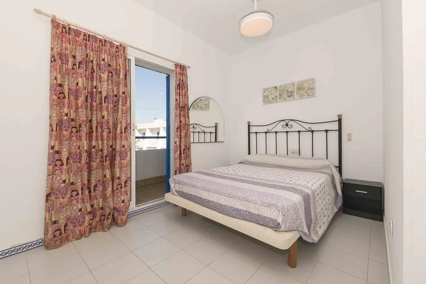 A bedroom with a metal-framed bed and patterned curtains beside a glass door.
